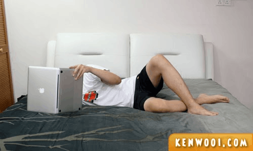 Man lying in bed on his side, using a MacBook sideways